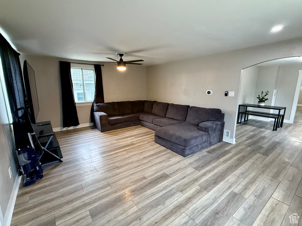 Living area with arched walkways, ceiling fan, and light wood-style floors