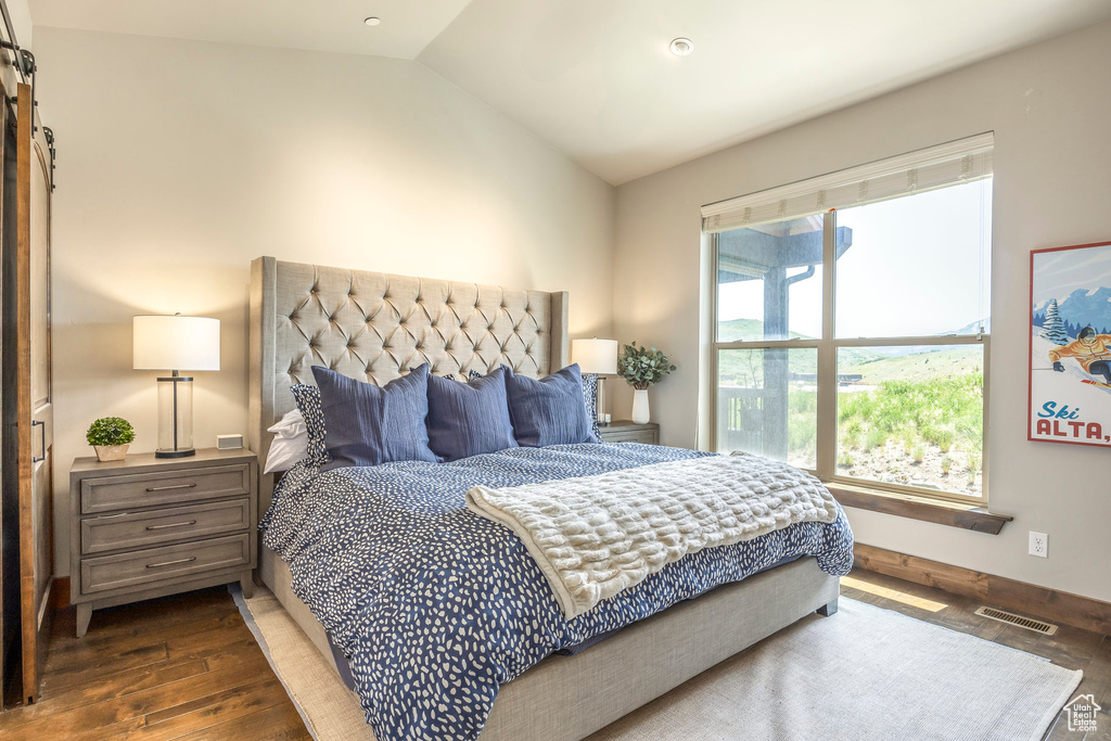 Bedroom featuring wood finished floors, vaulted ceiling, and a barn door