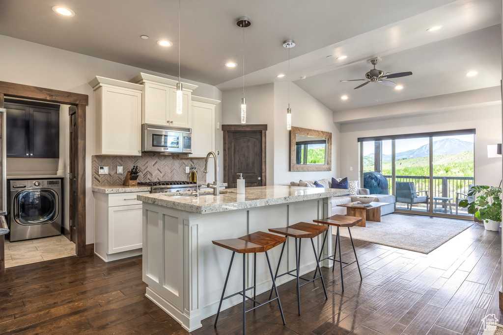 Kitchen with washer / clothes dryer, stainless steel microwave, open floor plan, dark wood-type flooring, and tasteful backsplash