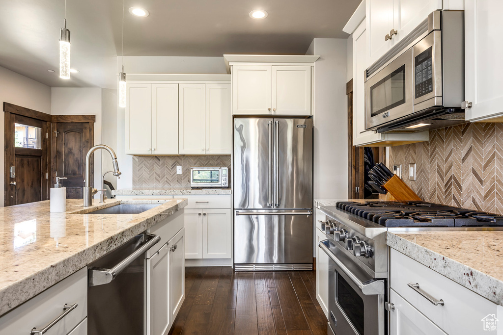 Kitchen with high end appliances, tasteful backsplash, recessed lighting, light stone counters, and white cabinets