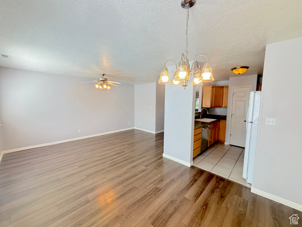 Kitchen featuring freestanding refrigerator, ceiling fan, light wood finished floors, stainless steel dishwasher, and a chandelier