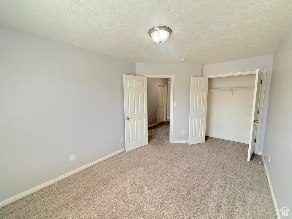 Unfurnished bedroom with light carpet, a textured ceiling, and a closet