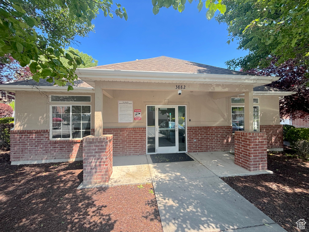 View of exterior entry with brick siding, stucco siding, roof with shingles, and a patio area