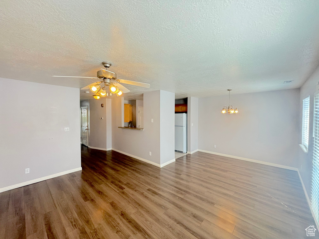 Unfurnished living room featuring a chandelier, a textured ceiling, wood finished floors, and a ceiling fan