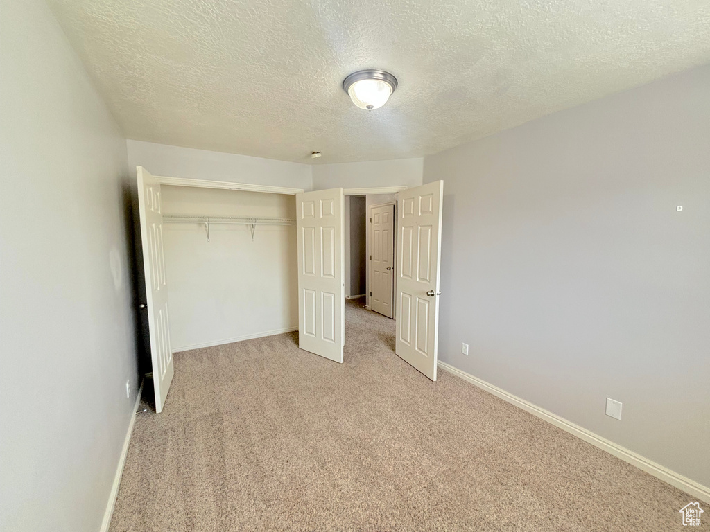 Unfurnished bedroom featuring a textured ceiling, a closet, and light colored carpet