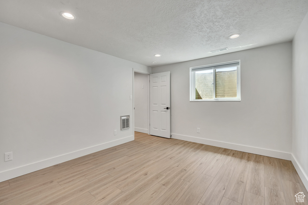 Empty room featuring a textured ceiling, light wood-style flooring, and recessed lighting