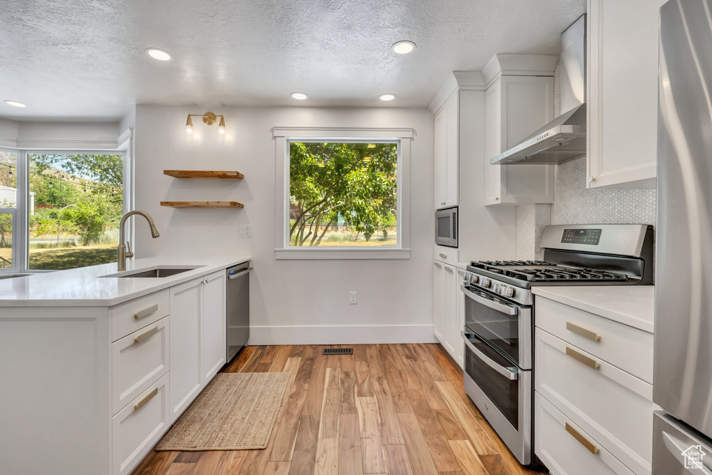 Kitchen featuring stainless steel appliances, wall chimney range hood, light countertops, white cabinets, and a textured ceiling