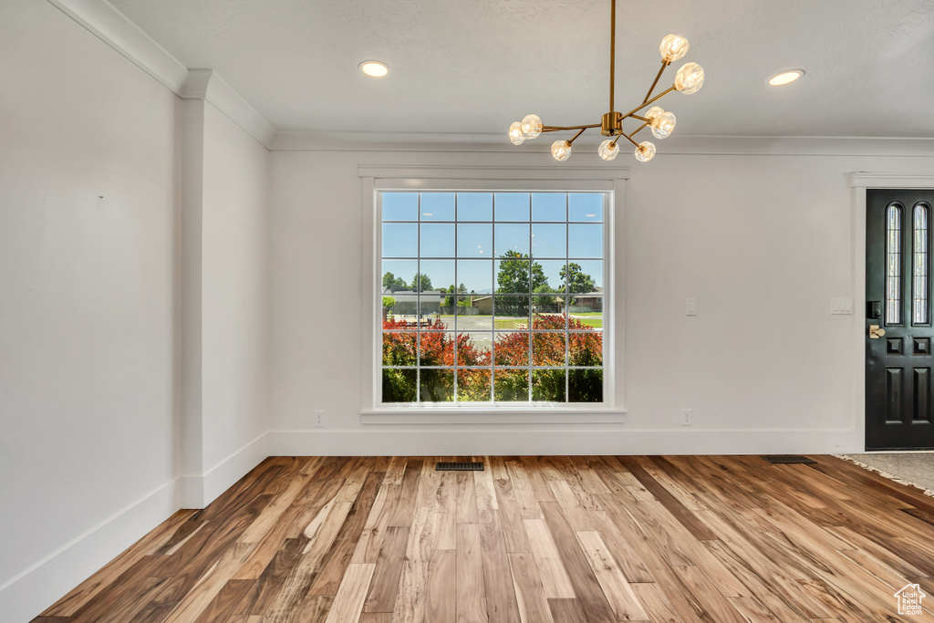 Unfurnished dining area with plenty of natural light, a chandelier, crown molding, wood finished floors, and recessed lighting