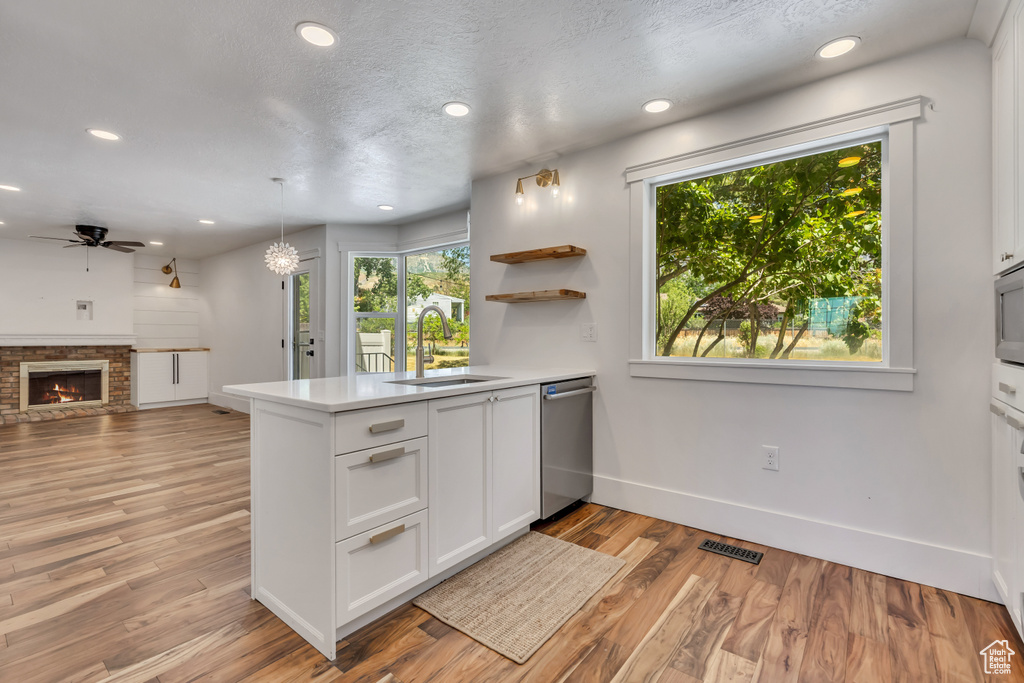 Kitchen featuring stainless steel appliances, a peninsula, a ceiling fan, white cabinets, and light wood-style floors