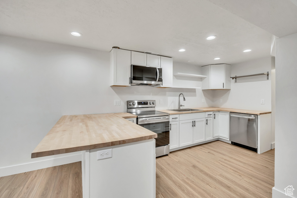 Kitchen featuring stainless steel appliances, wood counters, open shelves, a peninsula, and light wood-style flooring