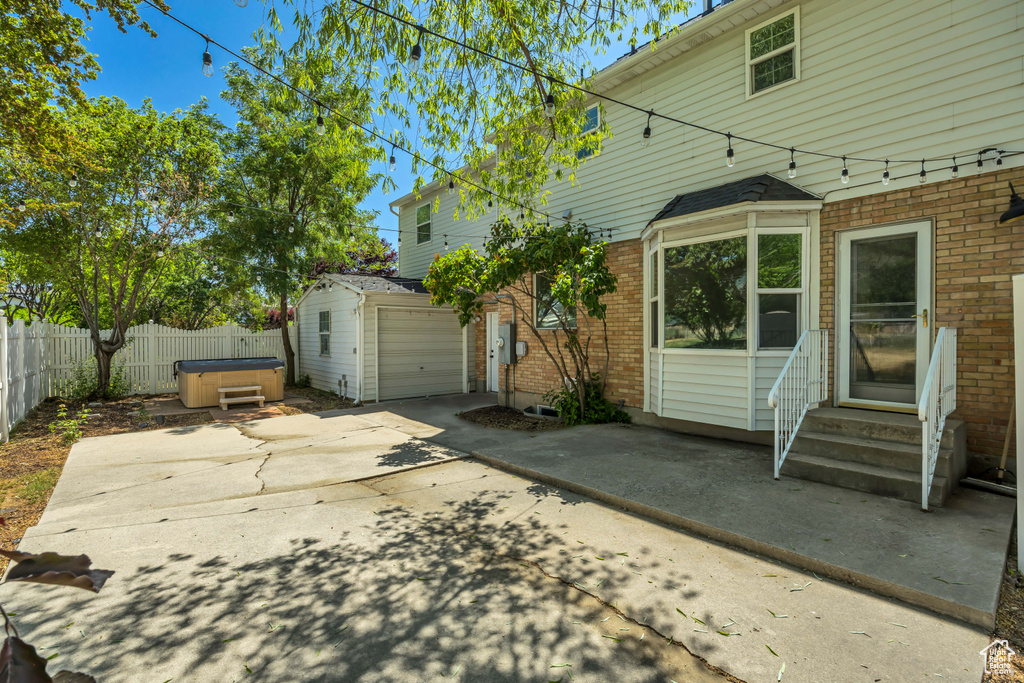 Fenced backyard with a hot tub, entry steps, a patio area, driveway, and a garage