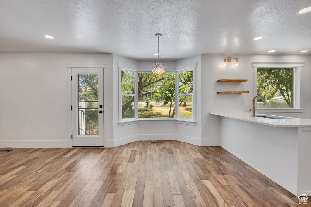 Unfurnished dining area with a textured ceiling, wood finished floors, recessed lighting, and a chandelier