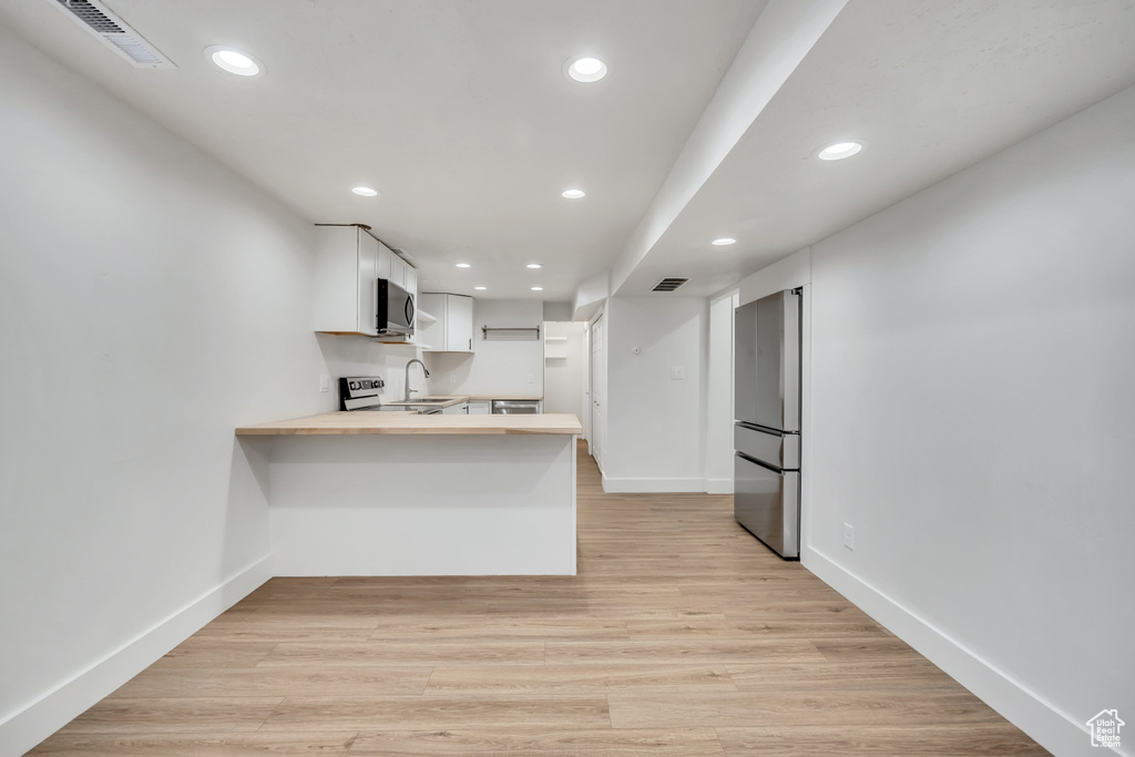 Kitchen featuring stainless steel appliances, a peninsula, butcher block counters, white cabinetry, and recessed lighting
