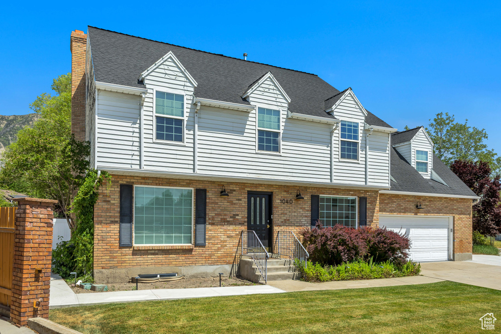 View of front of home with brick siding, a garage, driveway, and a front lawn