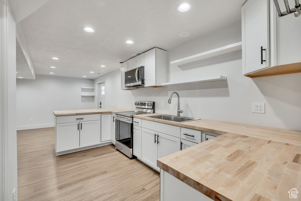 Kitchen with stainless steel appliances, open shelves, a peninsula, butcher block counters, and recessed lighting