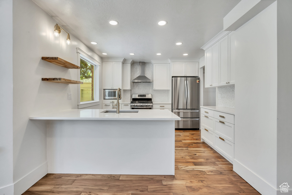 Kitchen with stainless steel appliances, wall chimney range hood, recessed lighting, a peninsula, and open shelves