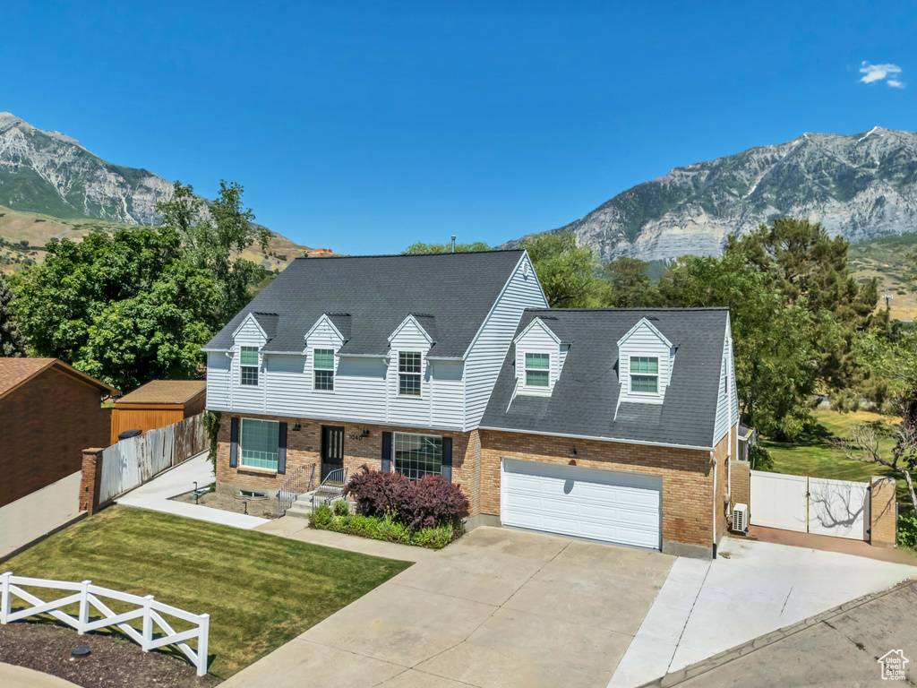 Cape cod home with brick siding, a gate, concrete driveway, a mountain view, and an attached garage