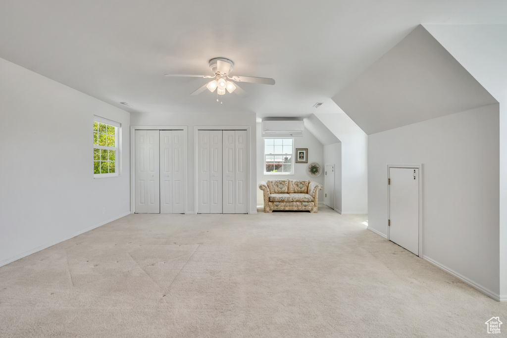 Unfurnished bedroom with a wall mounted air conditioner, two closets, light carpet, ceiling fan, and vaulted ceiling