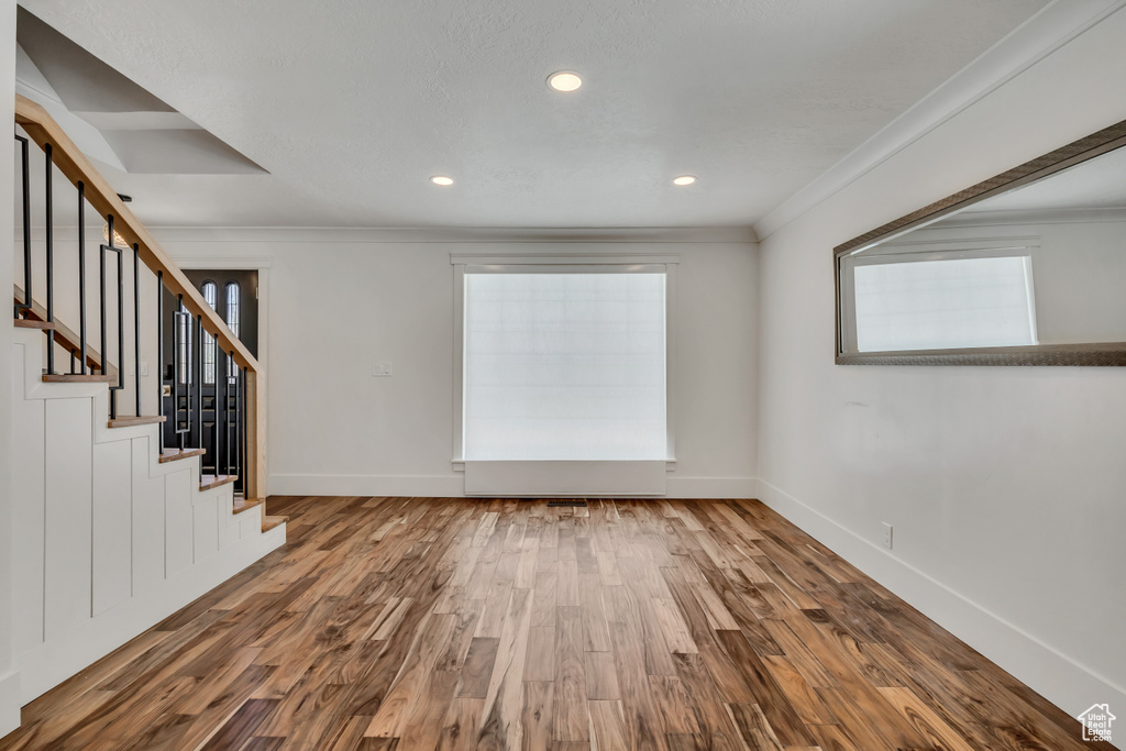 Unfurnished room featuring wood finished floors, ornamental molding, stairs, and recessed lighting