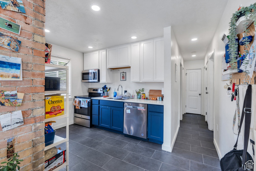 Kitchen featuring stainless steel appliances, blue cabinets, light countertops, dark tile patterned flooring, and recessed lighting