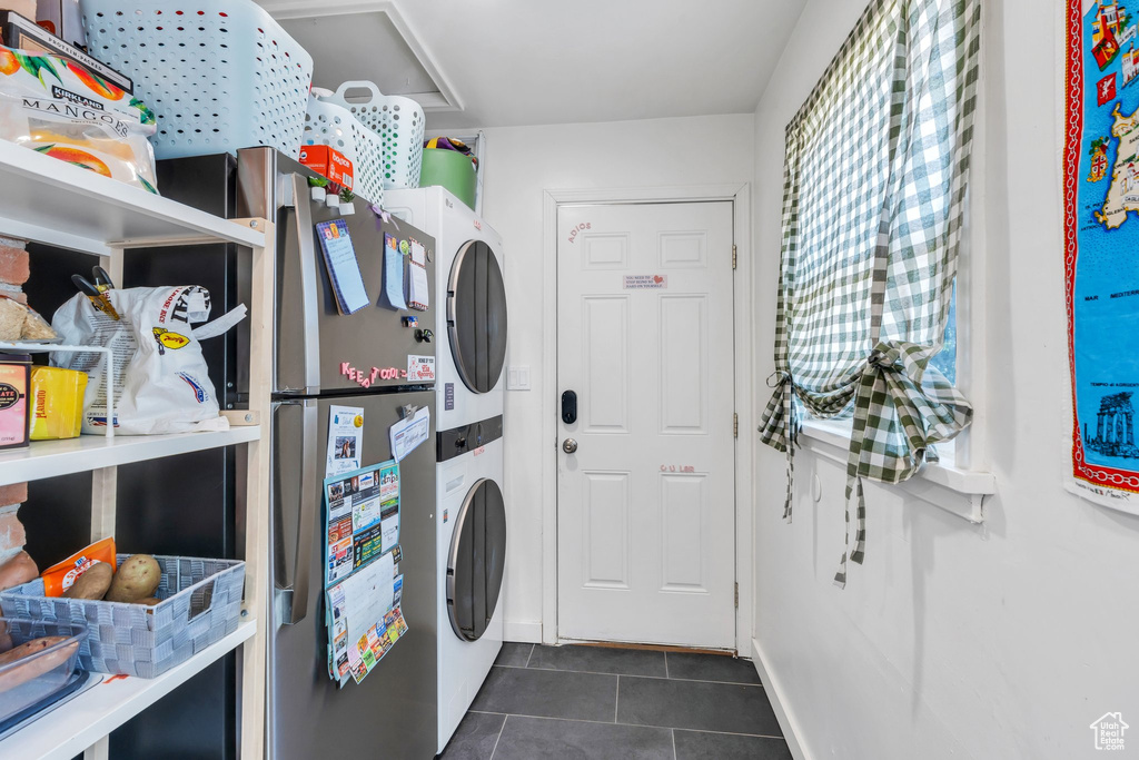 Washroom featuring stacked washing machine and dryer and dark tile patterned flooring