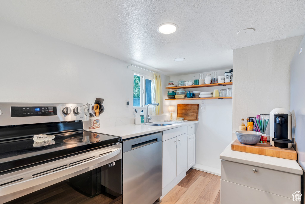 Kitchen featuring appliances with stainless steel finishes, open shelves, light countertops, white cabinetry, and a textured ceiling