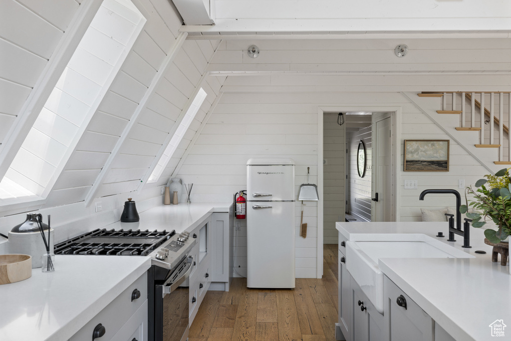 Kitchen with stainless steel gas range oven, freestanding refrigerator, light wood-style flooring, light countertops, and wooden walls
