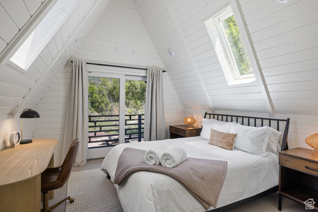 Carpeted bedroom featuring a skylight, vaulted ceiling, access to exterior, and wooden walls