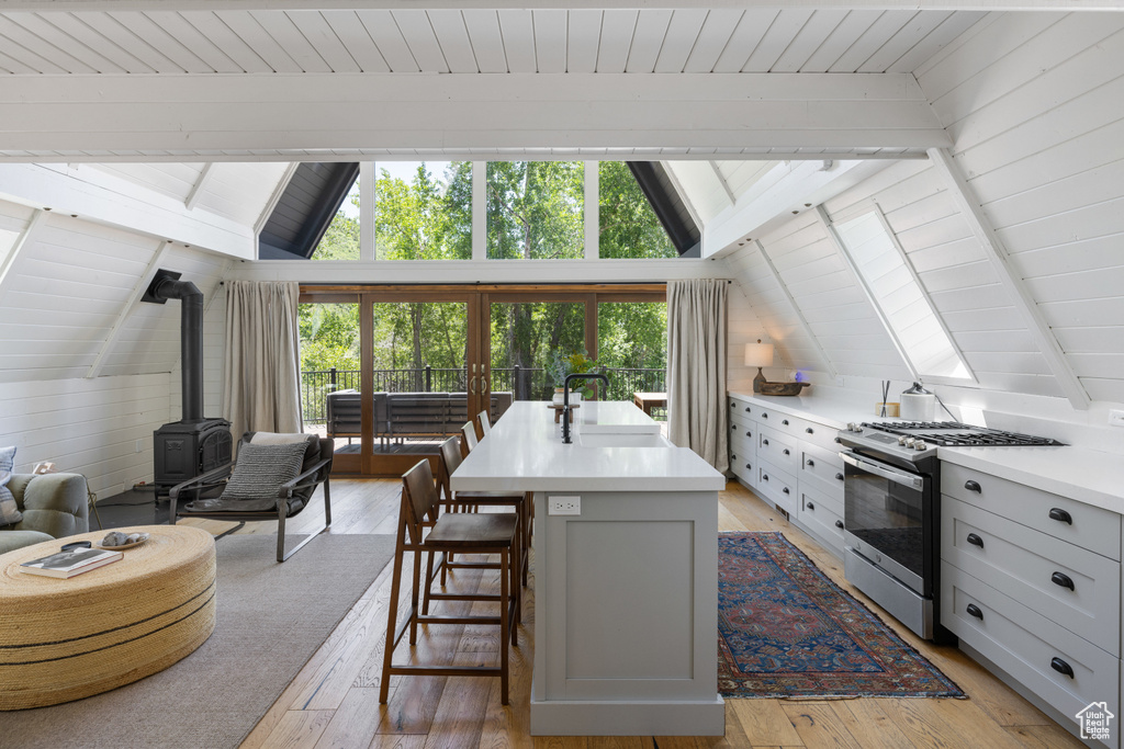 Kitchen with stainless steel range with gas stovetop, a wood stove, light countertops, a kitchen breakfast bar, and light wood finished floors