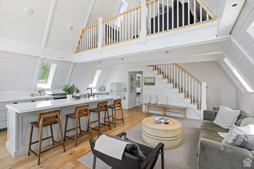 Living area with light wood-type flooring, high vaulted ceiling, stairs, wood walls, and beam ceiling