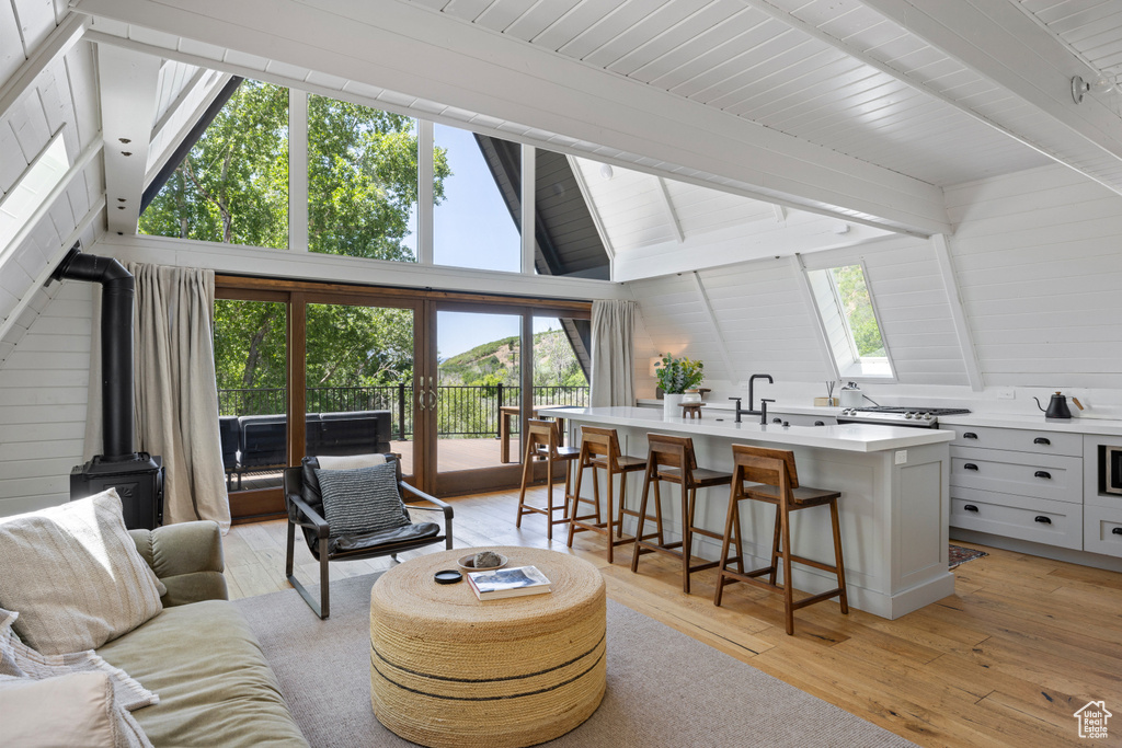 Living area with a wood stove, light wood-style floors, beamed ceiling, and high vaulted ceiling