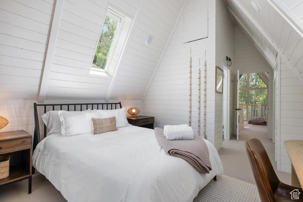 Bedroom with lofted ceiling, carpet, a skylight, wood walls, and access to exterior