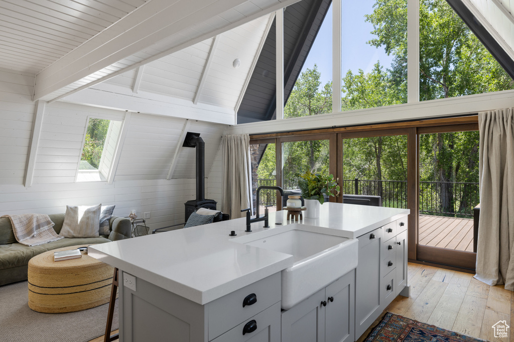 Kitchen with a wood stove, open floor plan, light countertops, beam ceiling, and an island with sink