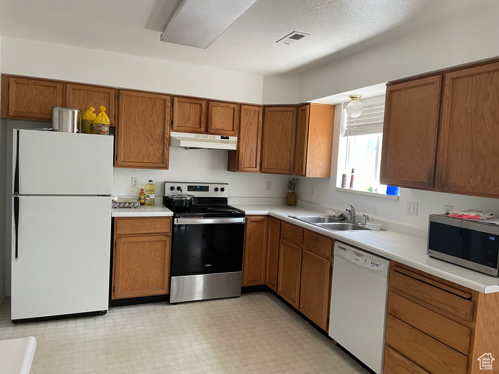 Kitchen featuring stainless steel appliances, under cabinet range hood, brown cabinets, and light countertops