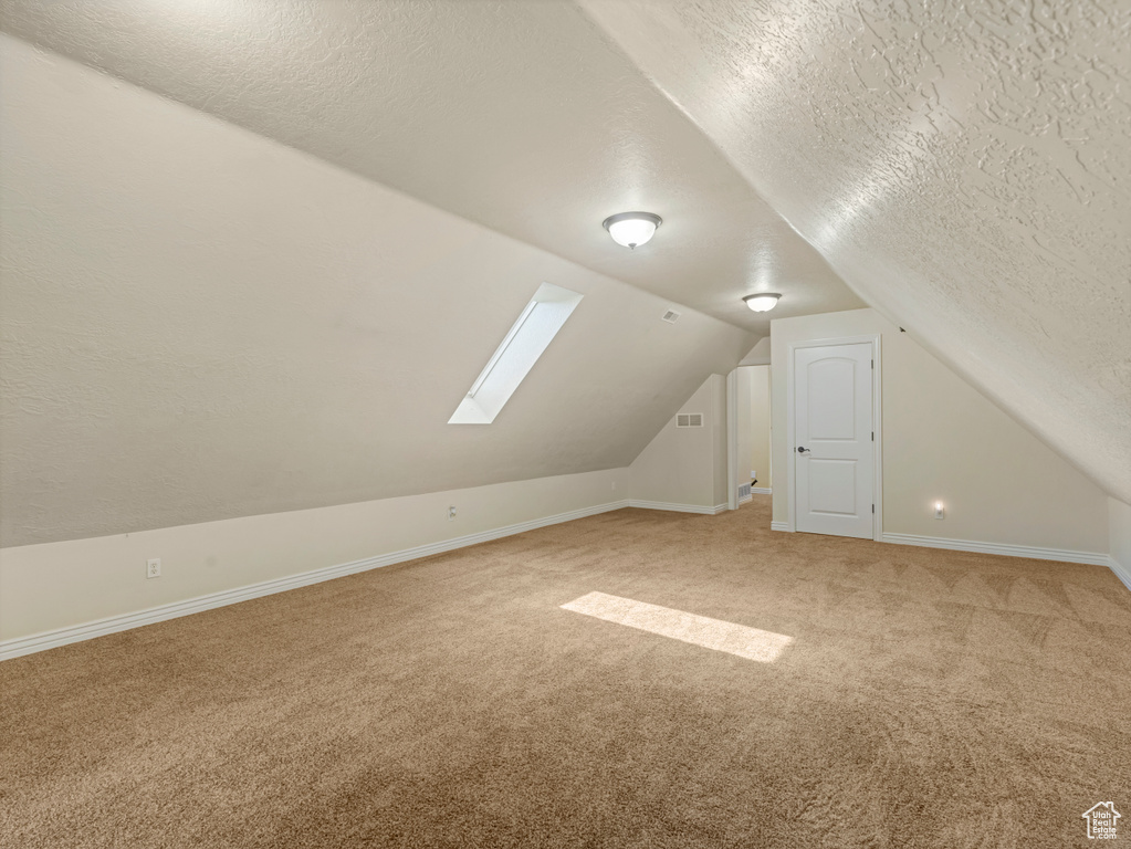 Additional living space featuring a textured ceiling, light colored carpet, lofted ceiling, and a skylight
