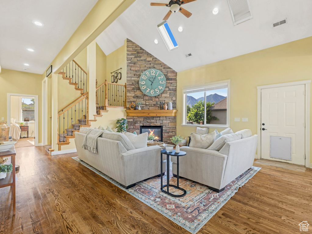 Living room with a ceiling fan, wood finished floors, high vaulted ceiling, stairway, and a fireplace