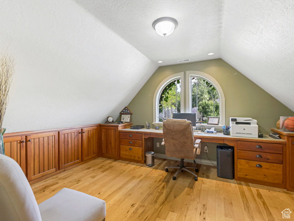 Office space with light wood-style floors, vaulted ceiling, and a textured ceiling