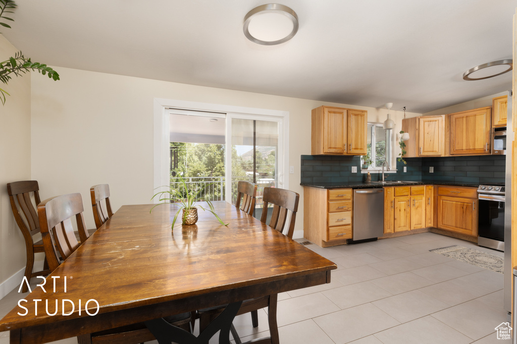 Kitchen featuring stainless steel appliances, tasteful backsplash, dark countertops, light brown cabinets, and light tile patterned floors