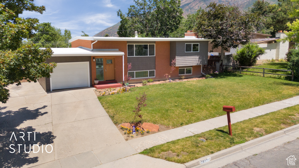 Bi-level home with a garage, driveway, a chimney, brick siding, and a mountain view