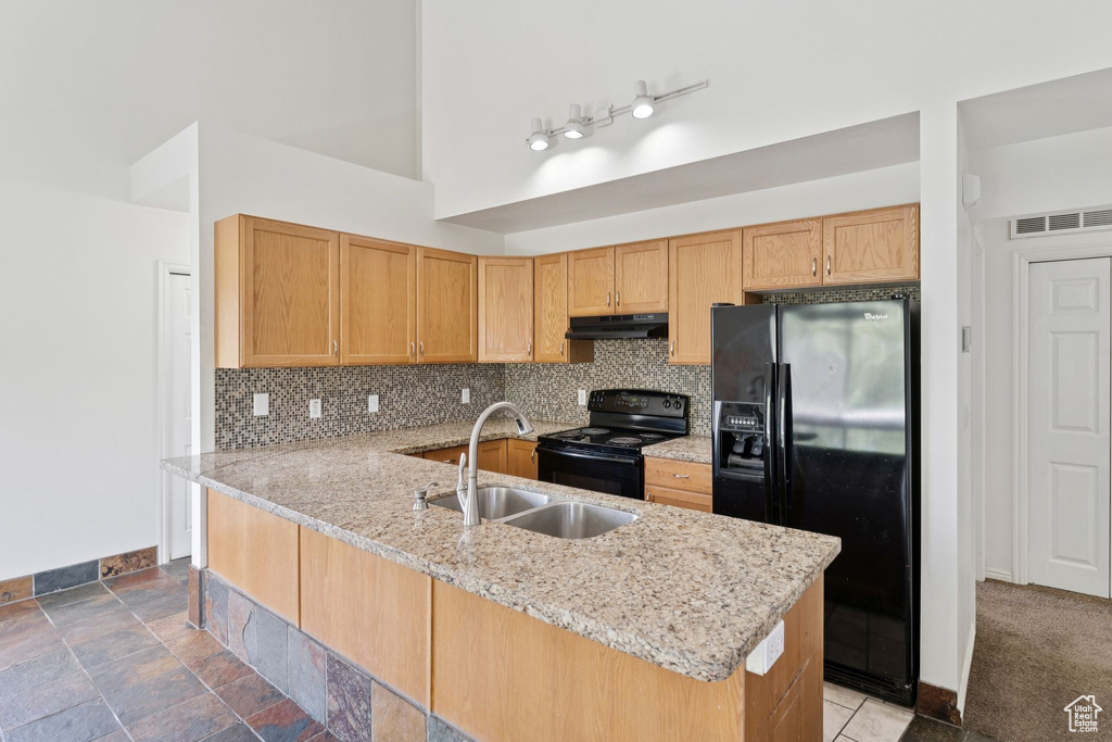 Kitchen featuring black appliances, under cabinet range hood, light stone counters, backsplash, and a towering ceiling