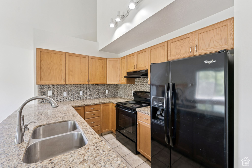Kitchen featuring black appliances, under cabinet range hood, tasteful backsplash, light stone countertops, and light tile patterned floors