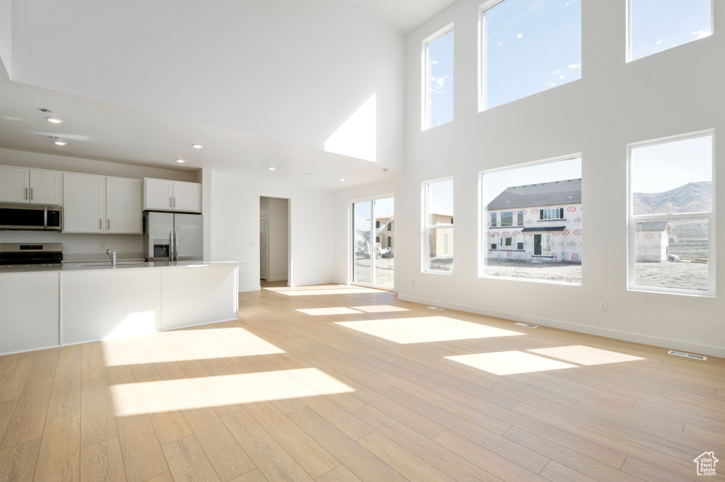 Unfurnished living room featuring light wood-style flooring and a towering ceiling