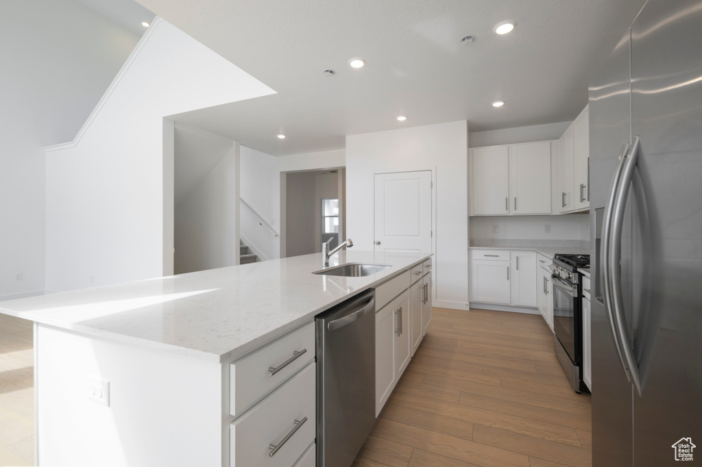 Kitchen with appliances with stainless steel finishes, light wood-style flooring, an island with sink, light stone countertops, and white cabinetry