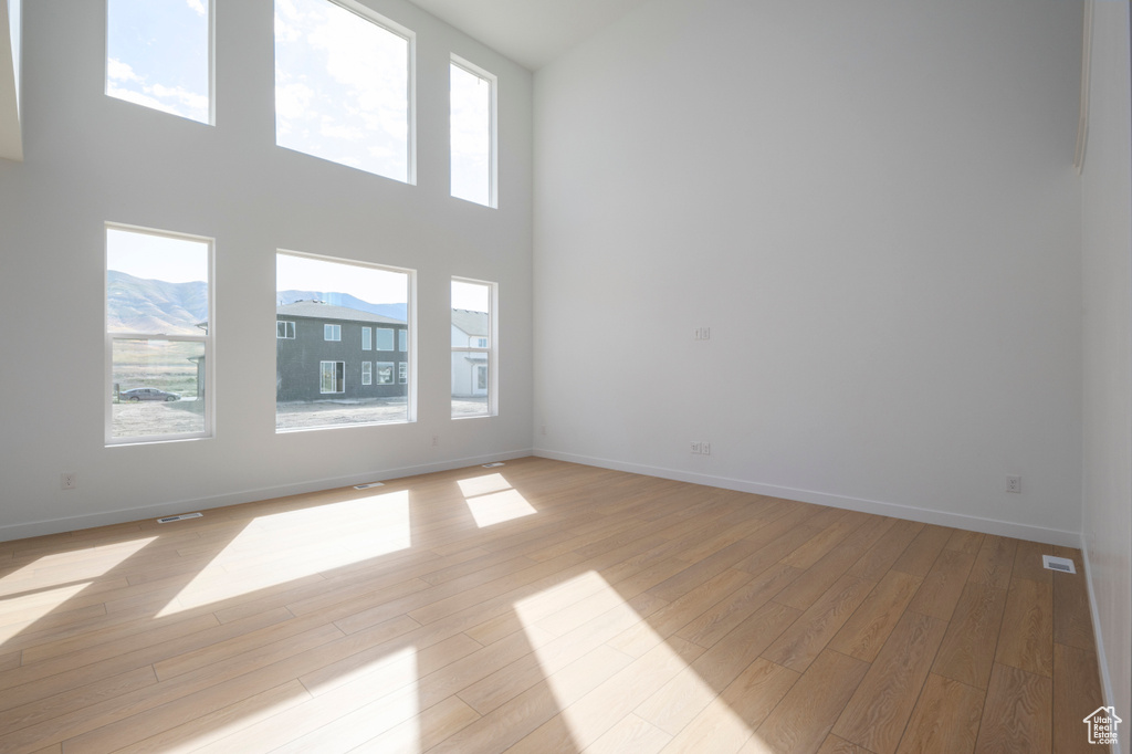 Empty room with plenty of natural light, light wood-style floors, and a towering ceiling