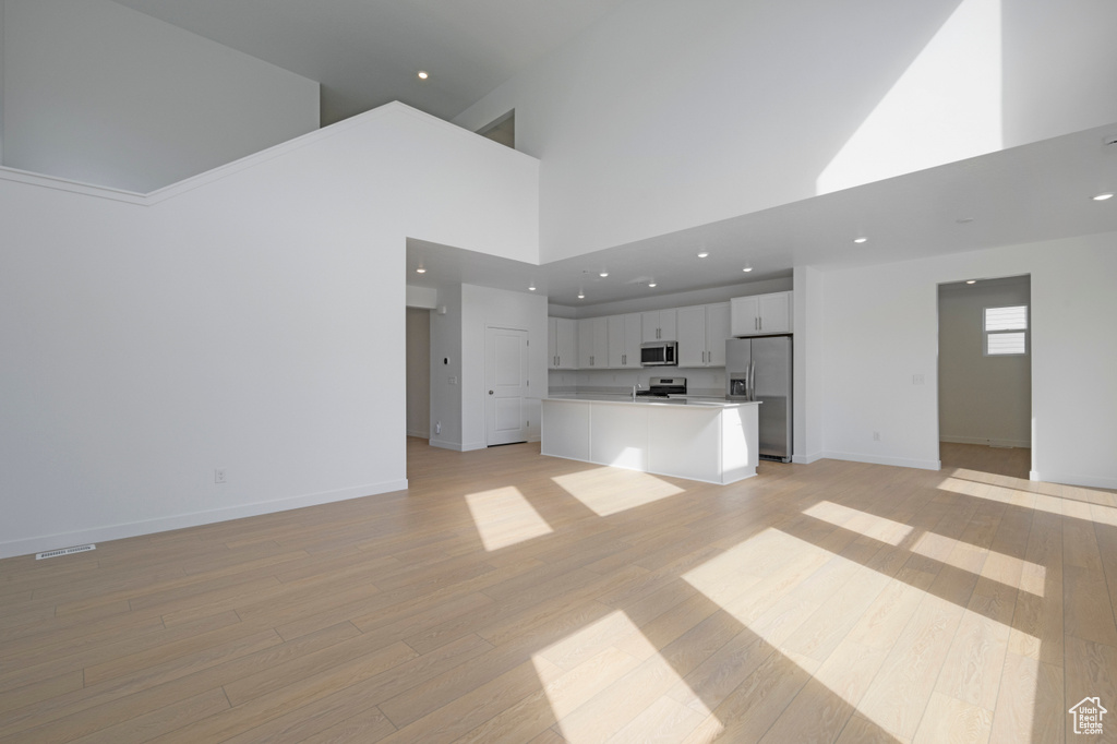 Unfurnished living room with a towering ceiling, light wood-style flooring, and recessed lighting