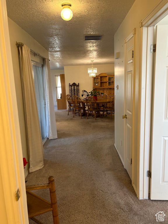 Hall with carpet flooring, a textured ceiling, and a chandelier