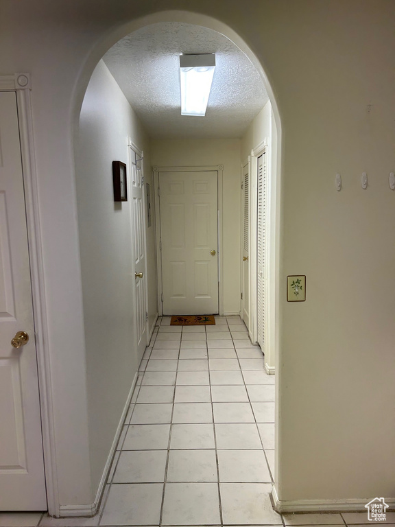 Hallway with arched walkways, a textured ceiling, light tile patterned flooring, and baseboards