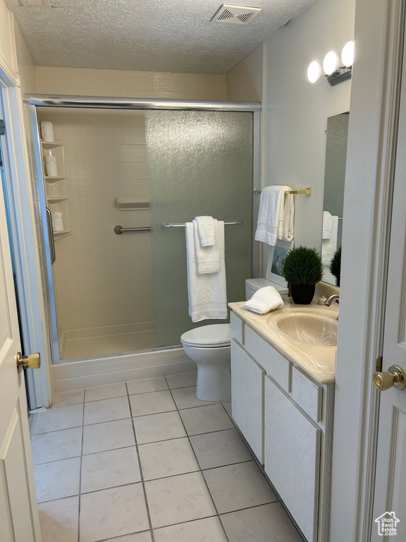 Bathroom with a stall shower, vanity, tile patterned flooring, toilet, and a textured ceiling