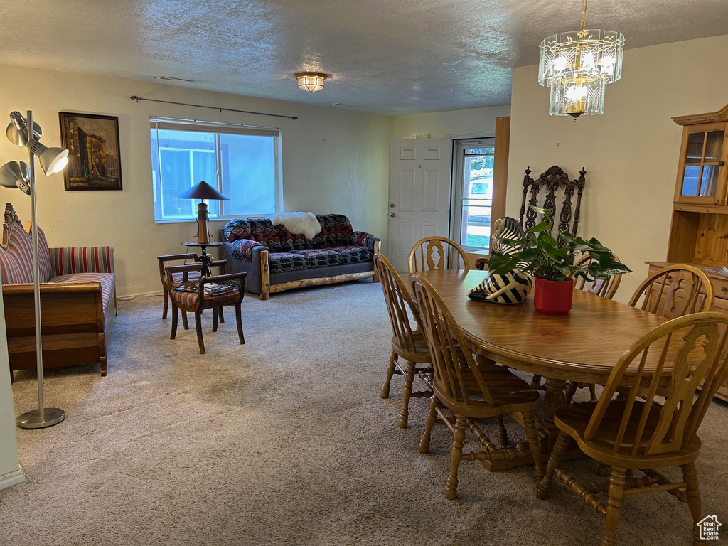 Dining room with healthy amount of natural light, carpet flooring, a textured ceiling, and a chandelier
