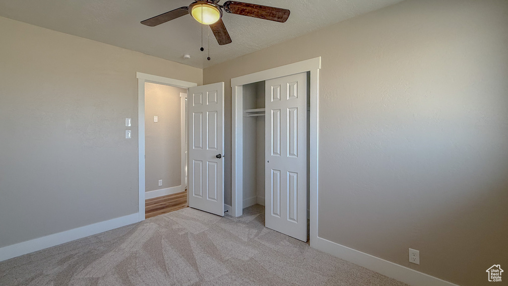 Unfurnished bedroom with light colored carpet, a closet, and a ceiling fan